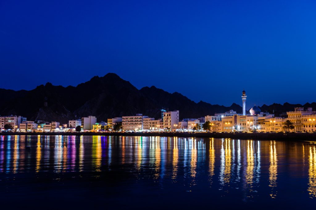The city of Muscat, waterfront lights, mountains behind, at night